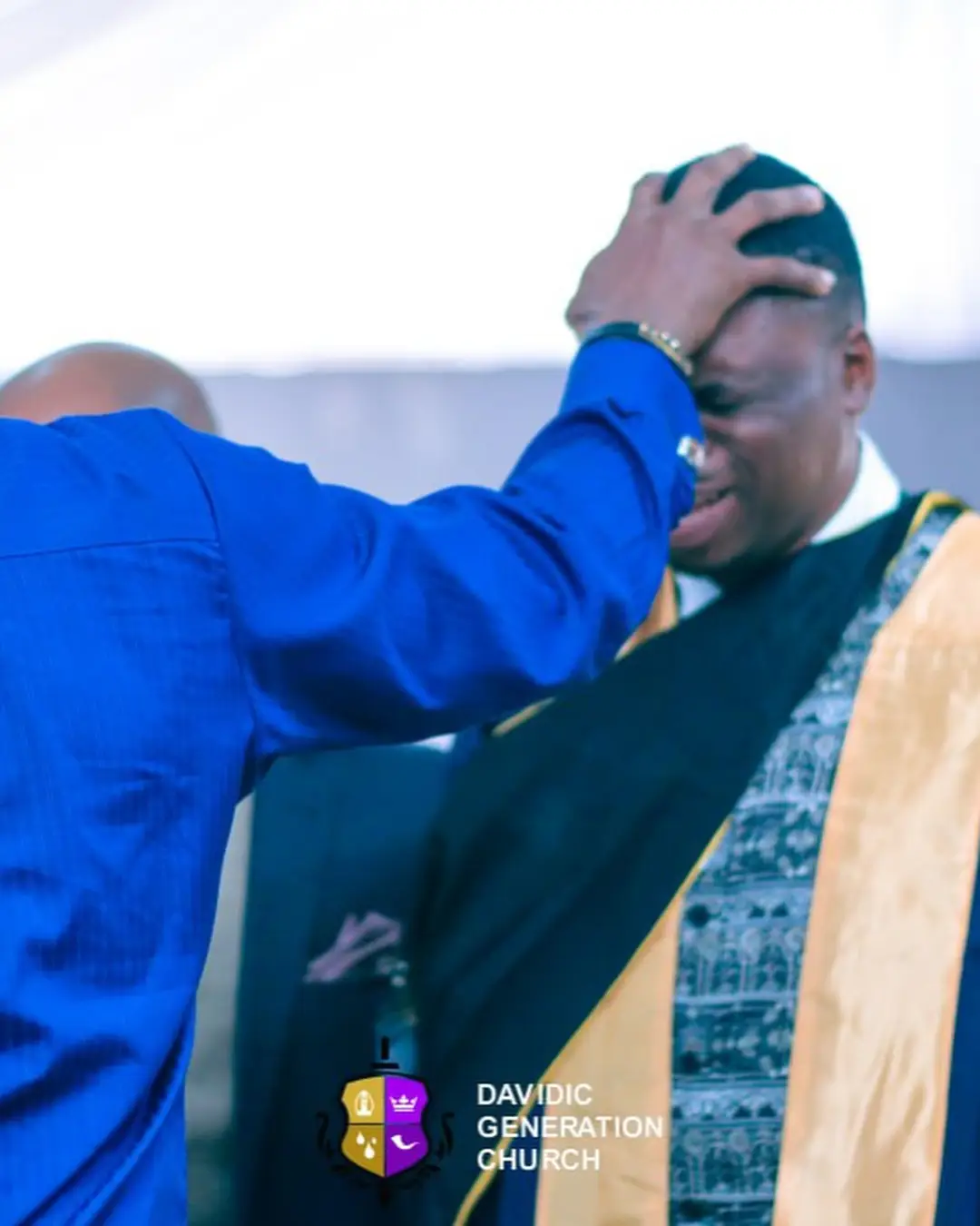A DGC minister praying over a graduate wearing an academic stole