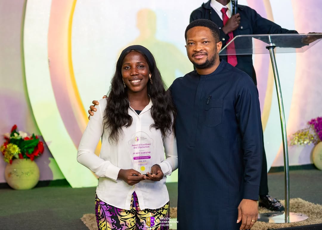 Pastor Godswill presenting an Award of Excellence and Distinction to a member on stage